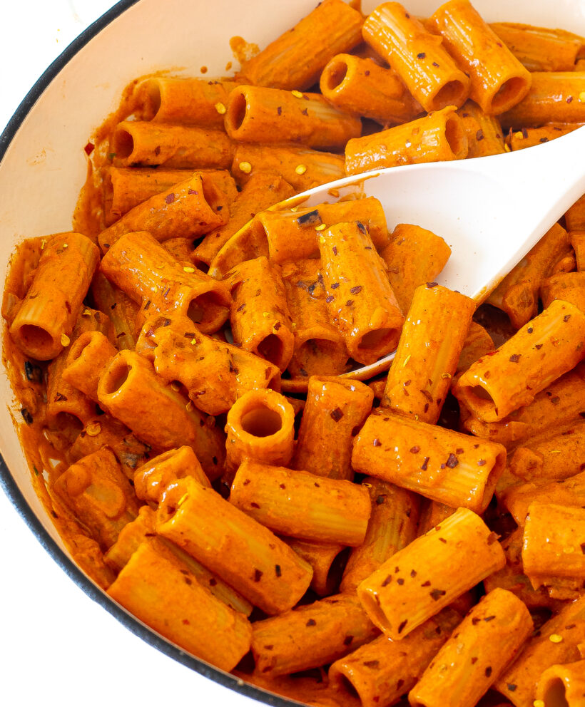Pasta in a bright red sauce in a skillet with crushed red pepper flakes on top. 