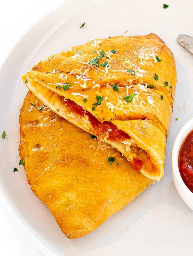 Calzone cut in half on a white plate with dipping sauce next to it.