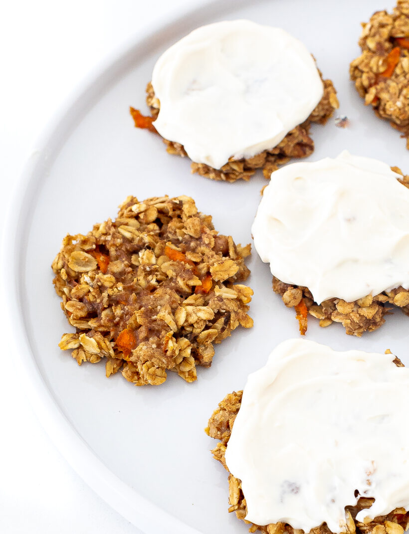 Healthy carrot cake cookies on a plate with some of the cookies topped with frosting. 