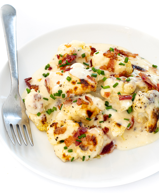 Cauliflower bake topped with bacon and chives on a white plate.
