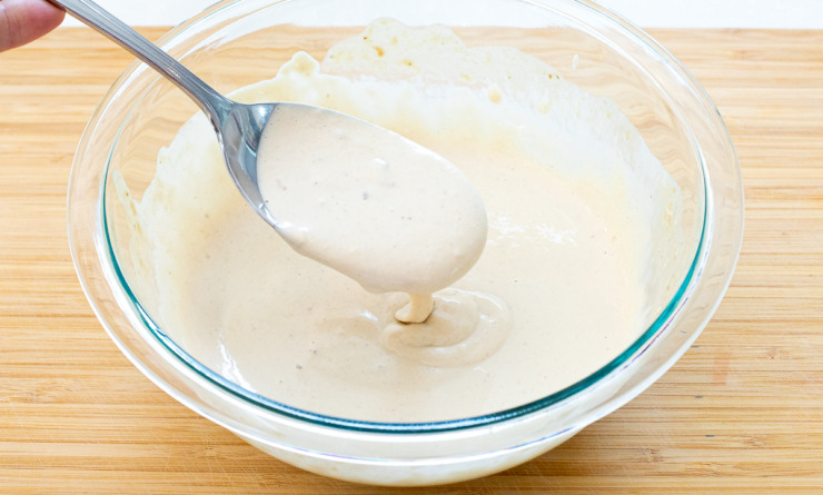 Caesar dressing in a clear mixing bowl with a spoon.