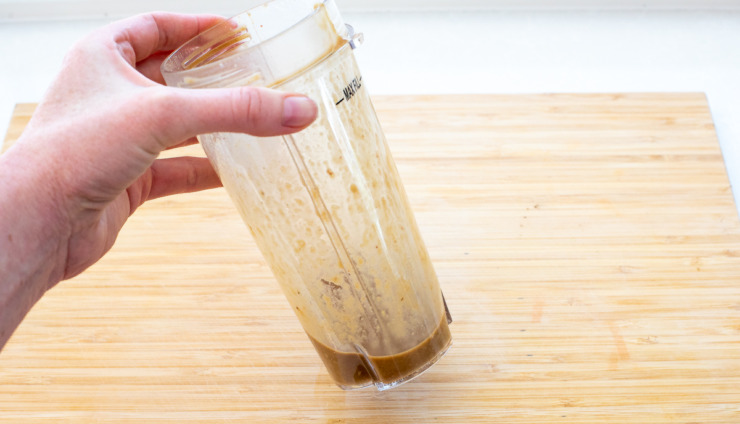 Hand holding anchovy sauce in a blender.
