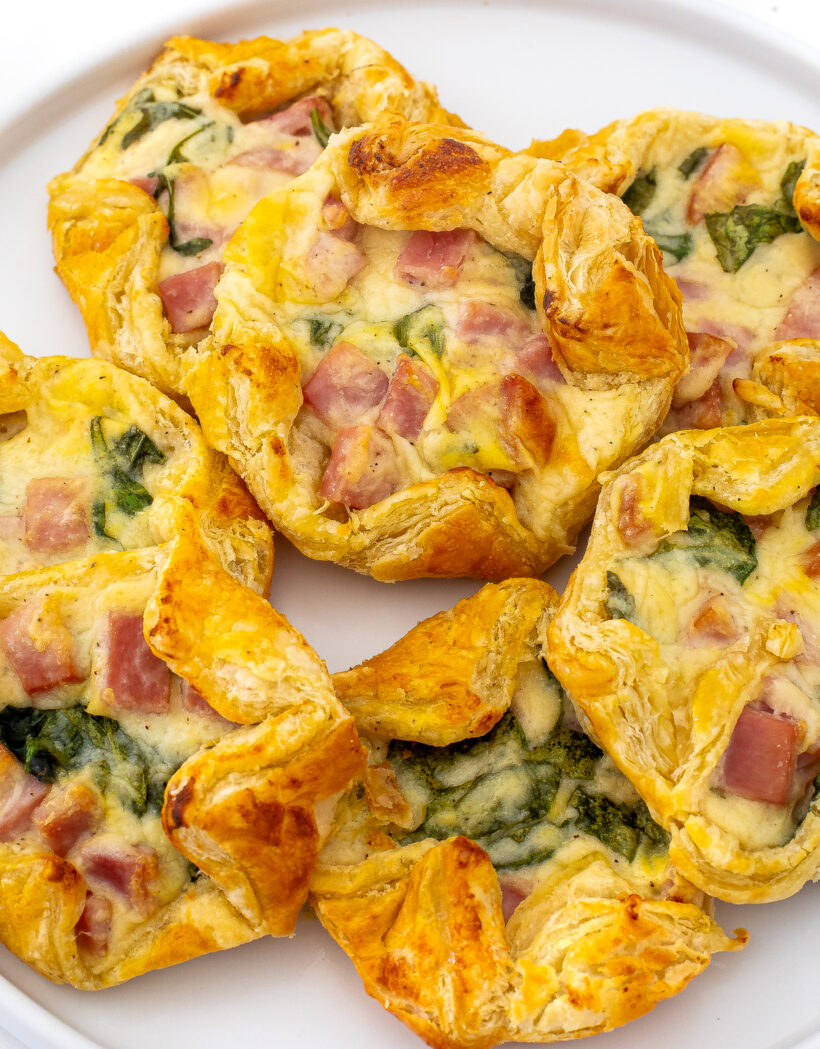 Ham and cheese puff pastries layered on top of each other and served on a white plate. 