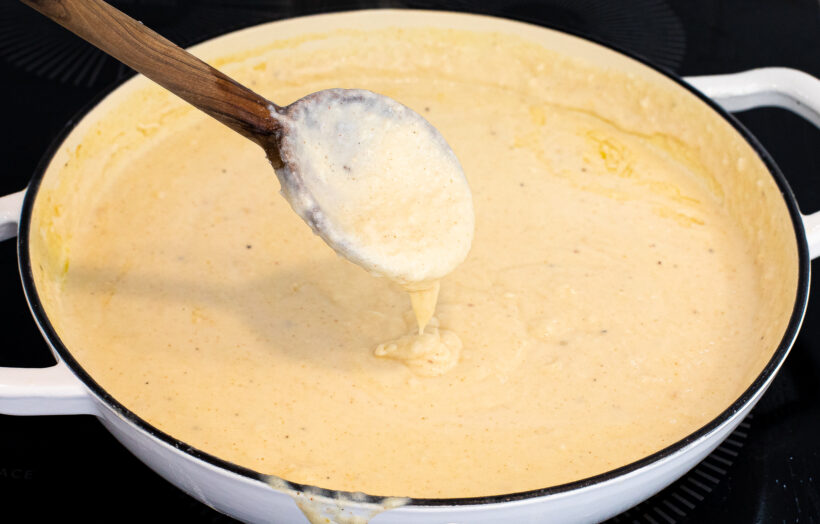 Cheese sauce being stirred with a wooden spoon.