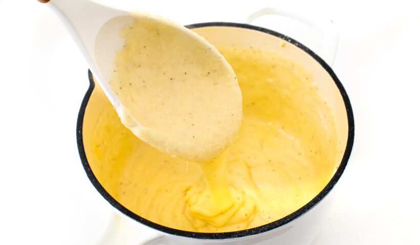 Cheese sauce in a saucepan with a white spoon. 