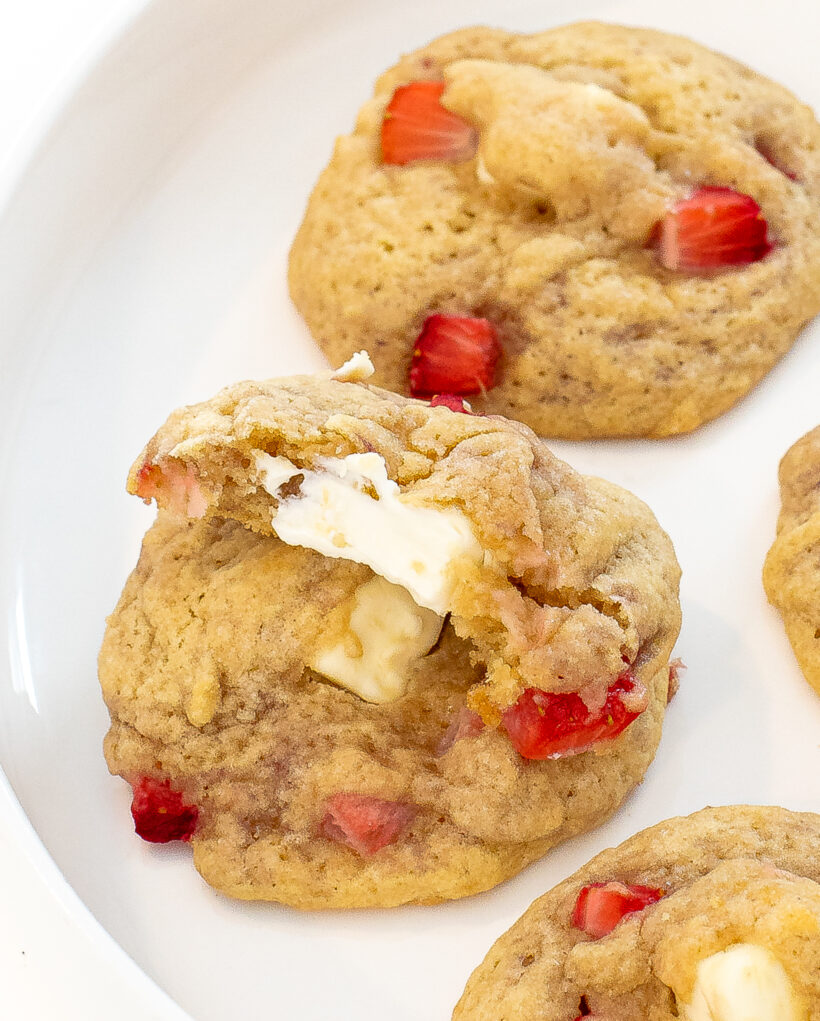 Strawberry cheesecake cookies stacked on top of each other with the top cookie missing a bite.