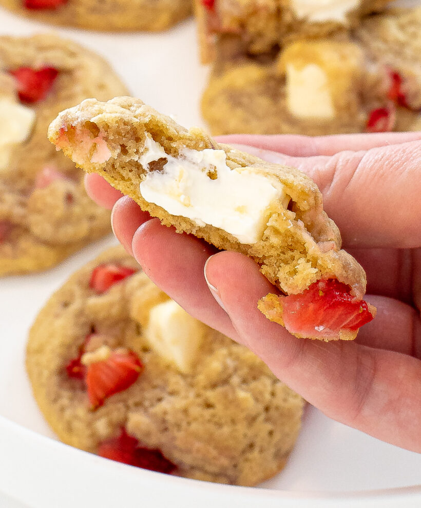 Hand holding a cookie with a bite taken out of it with more cookies in the background.