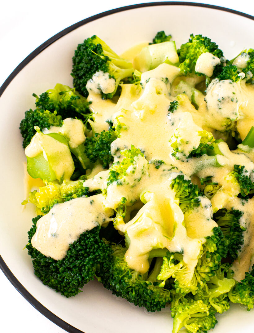 Broccoli topped with cheese sauce in a white and black serving bowl.