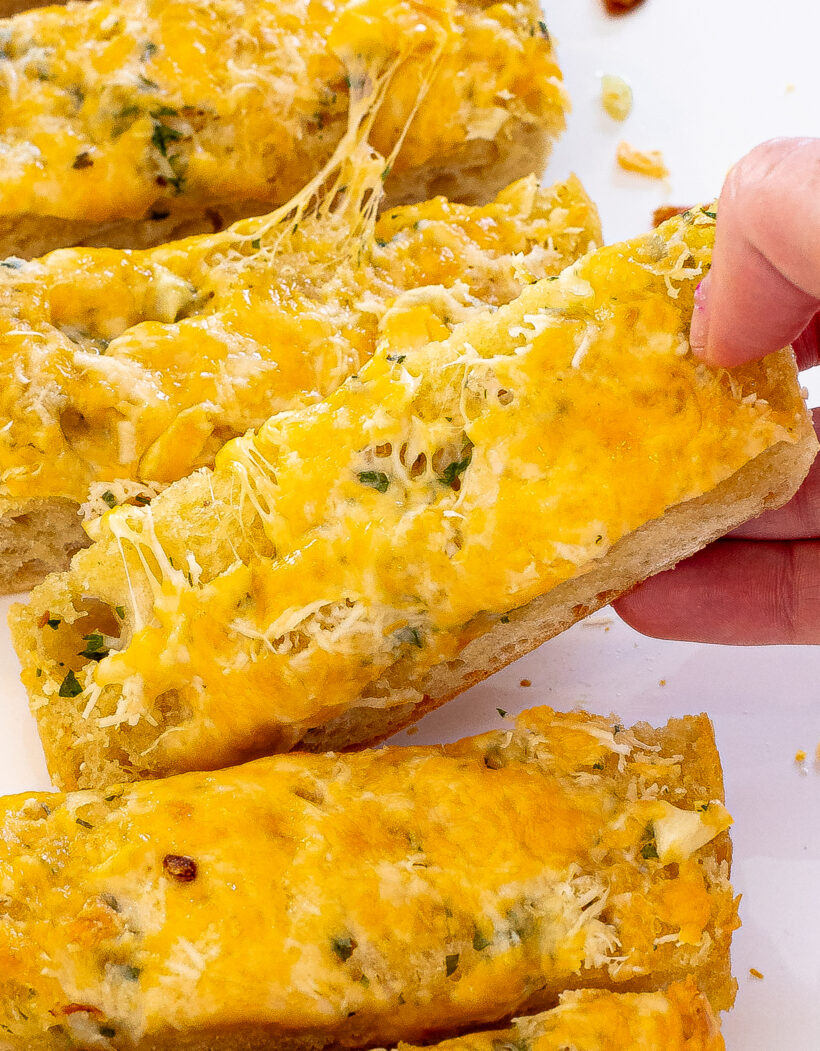 Slices of garlic bread with a hand grabbing one piece. 