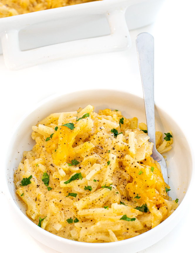 Hashbrown casserole in a white bowl with a silver spoon. 