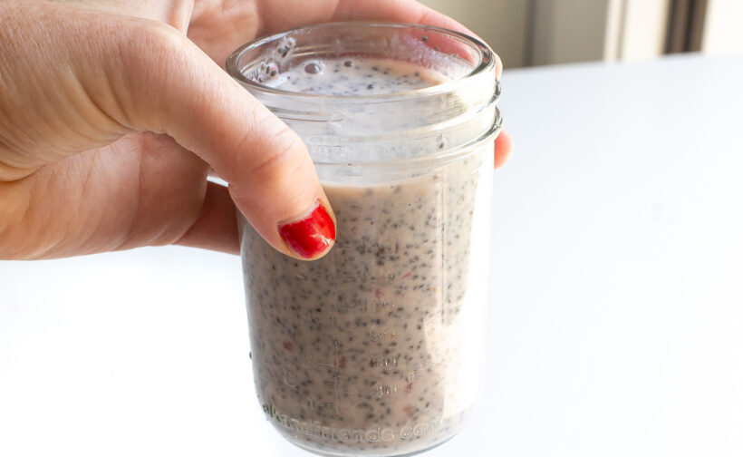 Hand holding a jar with raspberry chia pudding before it is chilled and set.
