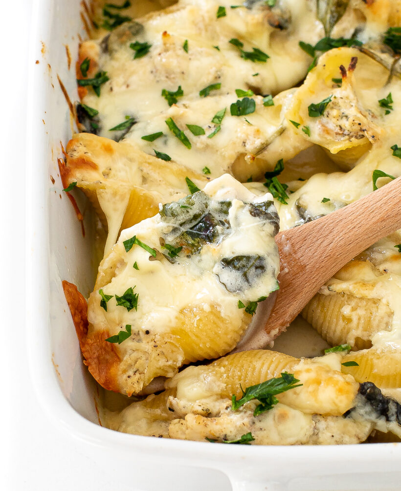 Alfred stuffed shells in a baking dish with a wooden spoon lifting one out of the dish. 