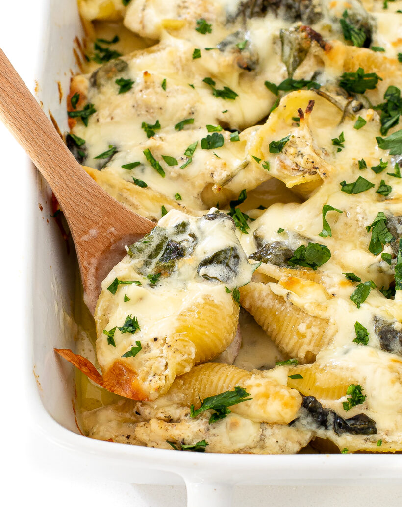Stuffed shells in a baking dish with a wooden spoon taking one out. 