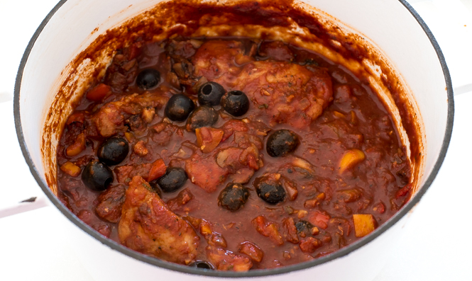 Mix olives into the red sauce with chicken in a white pot.