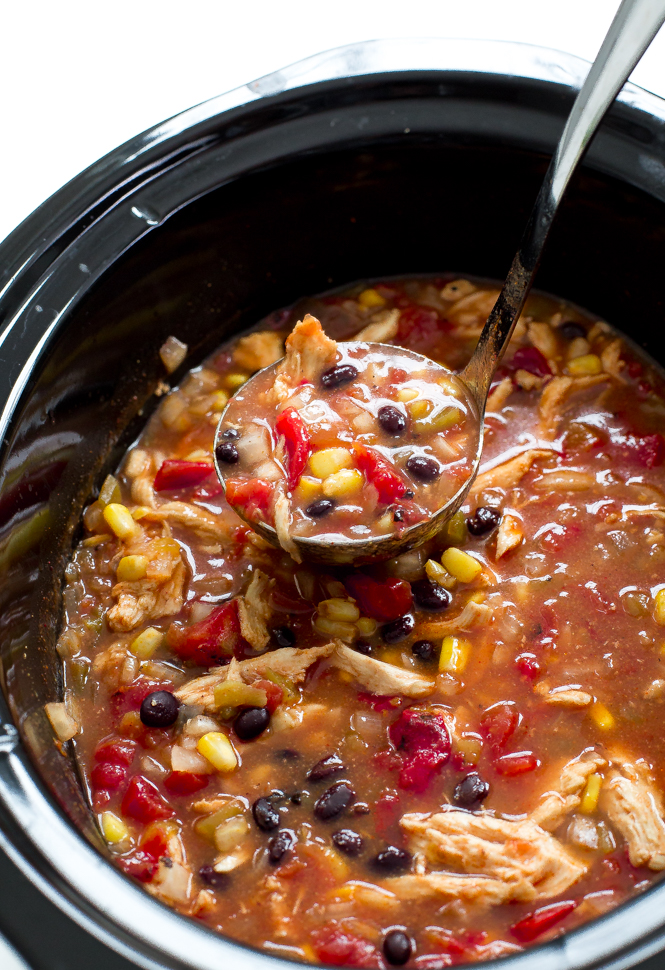 Shredded chicken enchilada soup in black slow cooker with ladle