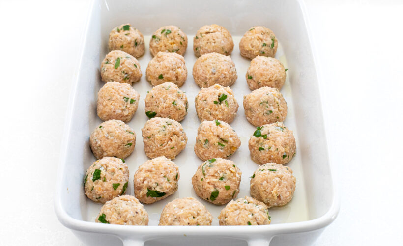 Raw chicken meatballs in a white baking dish. 