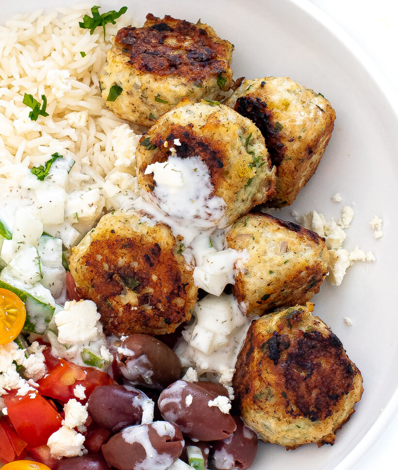 Chicken meatballs next to rice with tzatziki sauce drizzled on top.