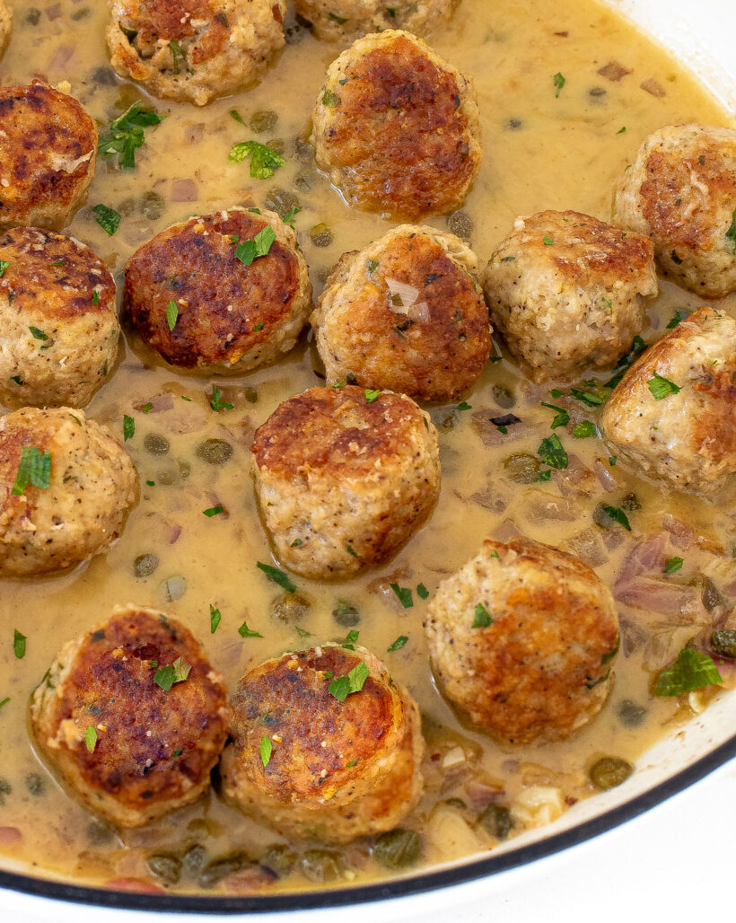 Chicken meatballs bathed in a piccata sauce in a white skillet.