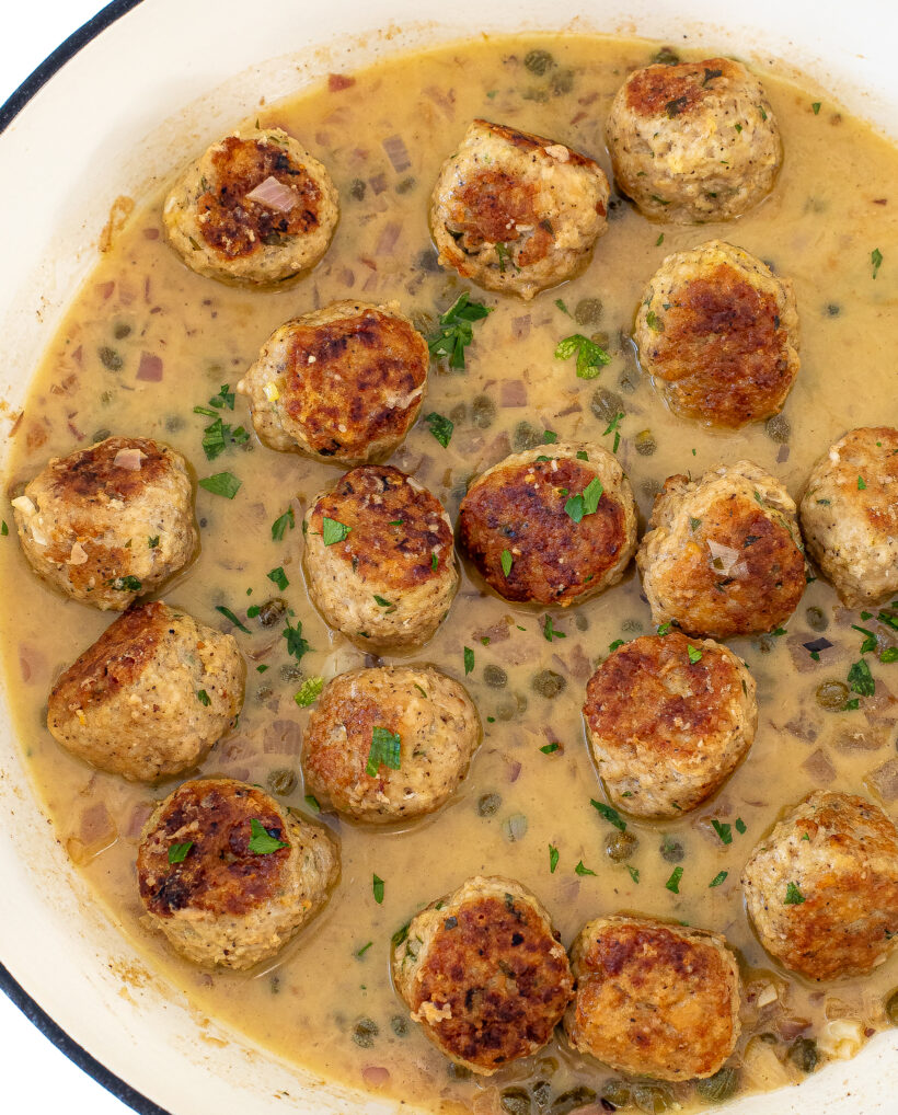 Overhead shot of chicken piccata meatballs in a skillet with sauce.