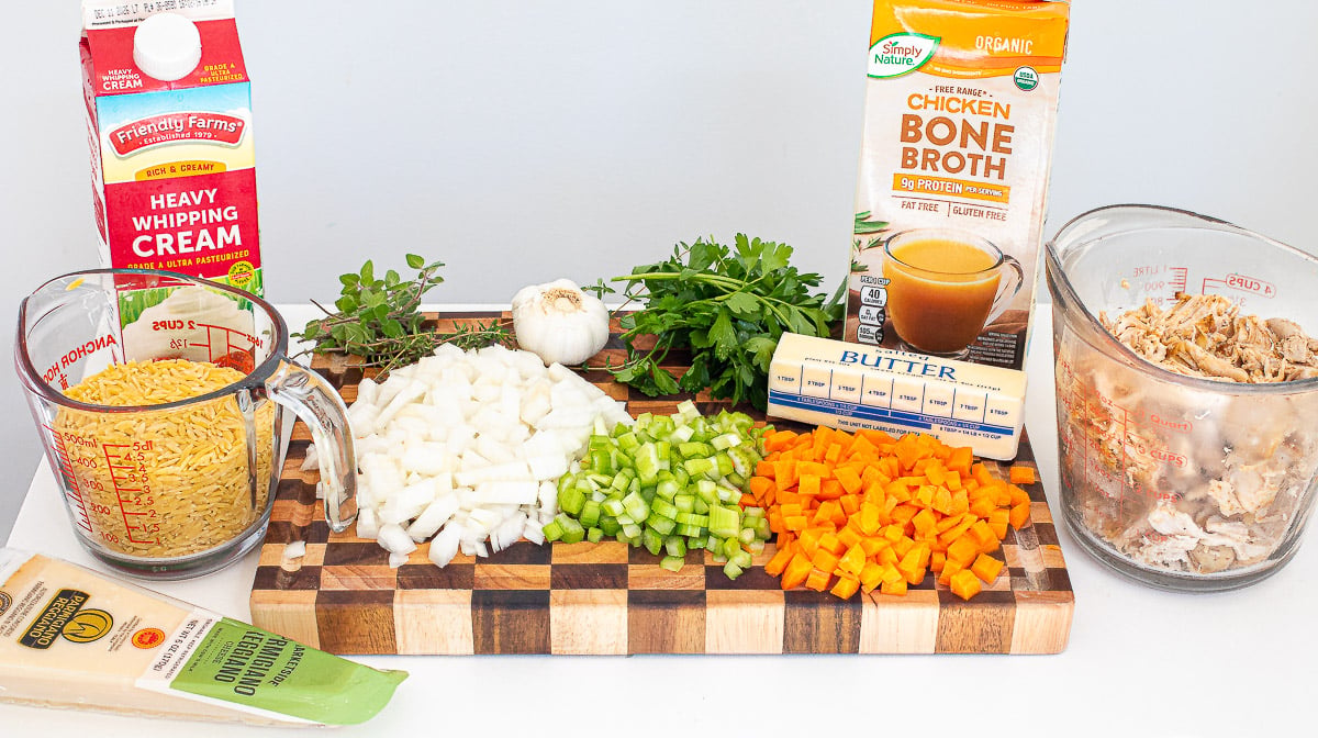Chopped carrots, onion and celery near bone broth, butter and fresh herbs.