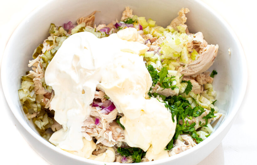 Ingredients for chicken salad in a white bowl.
