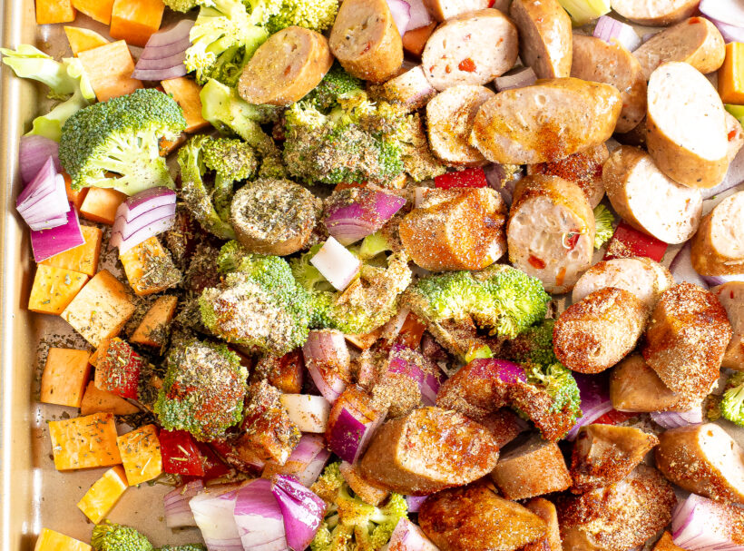 Diced veggies and sausage on a sheet pan topped with seasonings. 