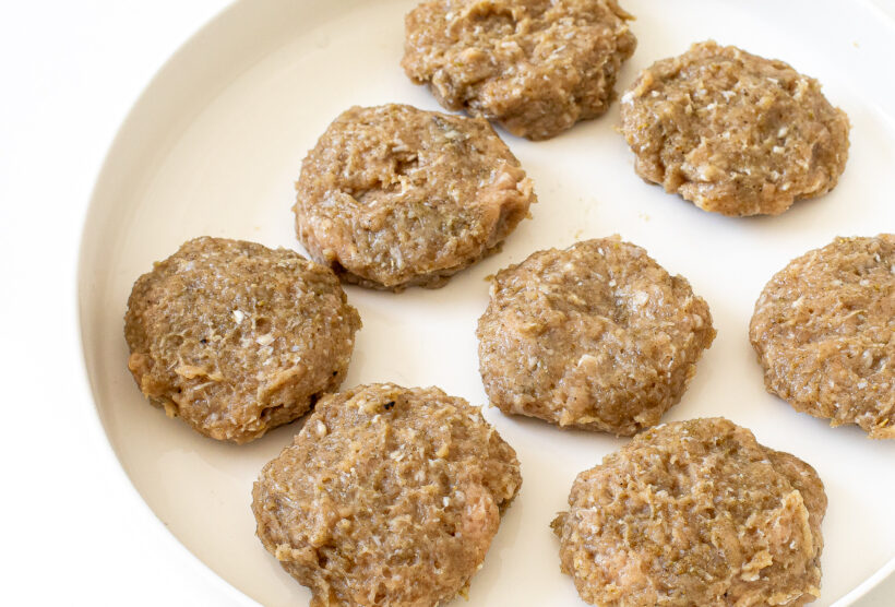 Uncooked breakfast sausages on a white plate.