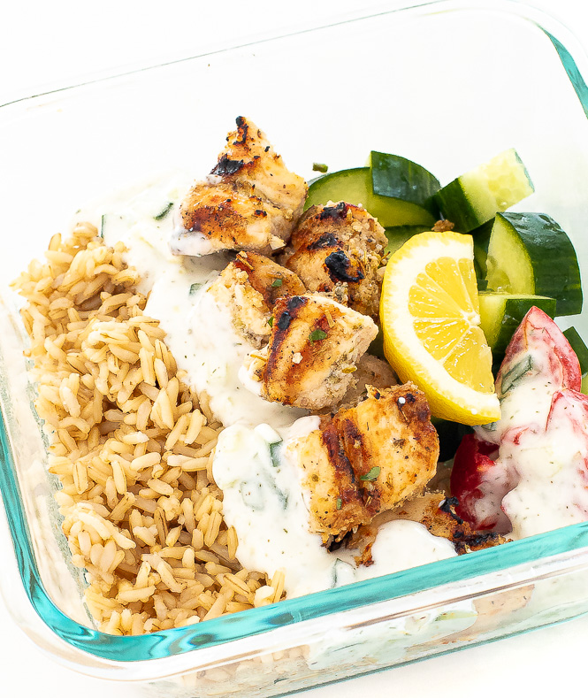 Glass container with rice, tzatziki sauce, chicken, and vegetables.