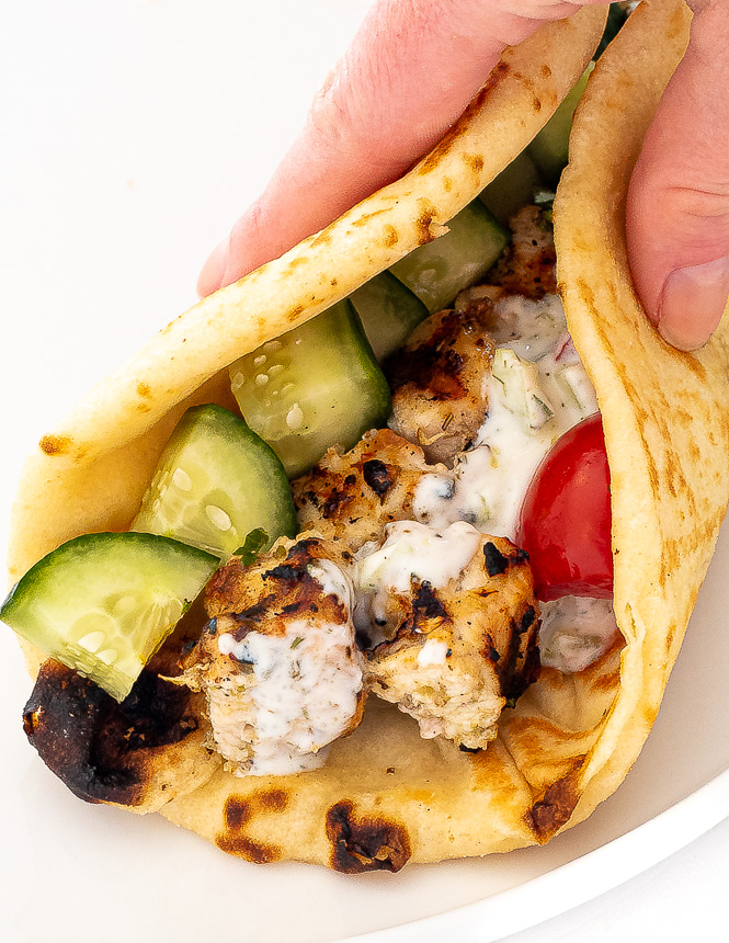 Hand holding a pita filled with chicken, cucumbers, tomatoes and tzatziki sauce.