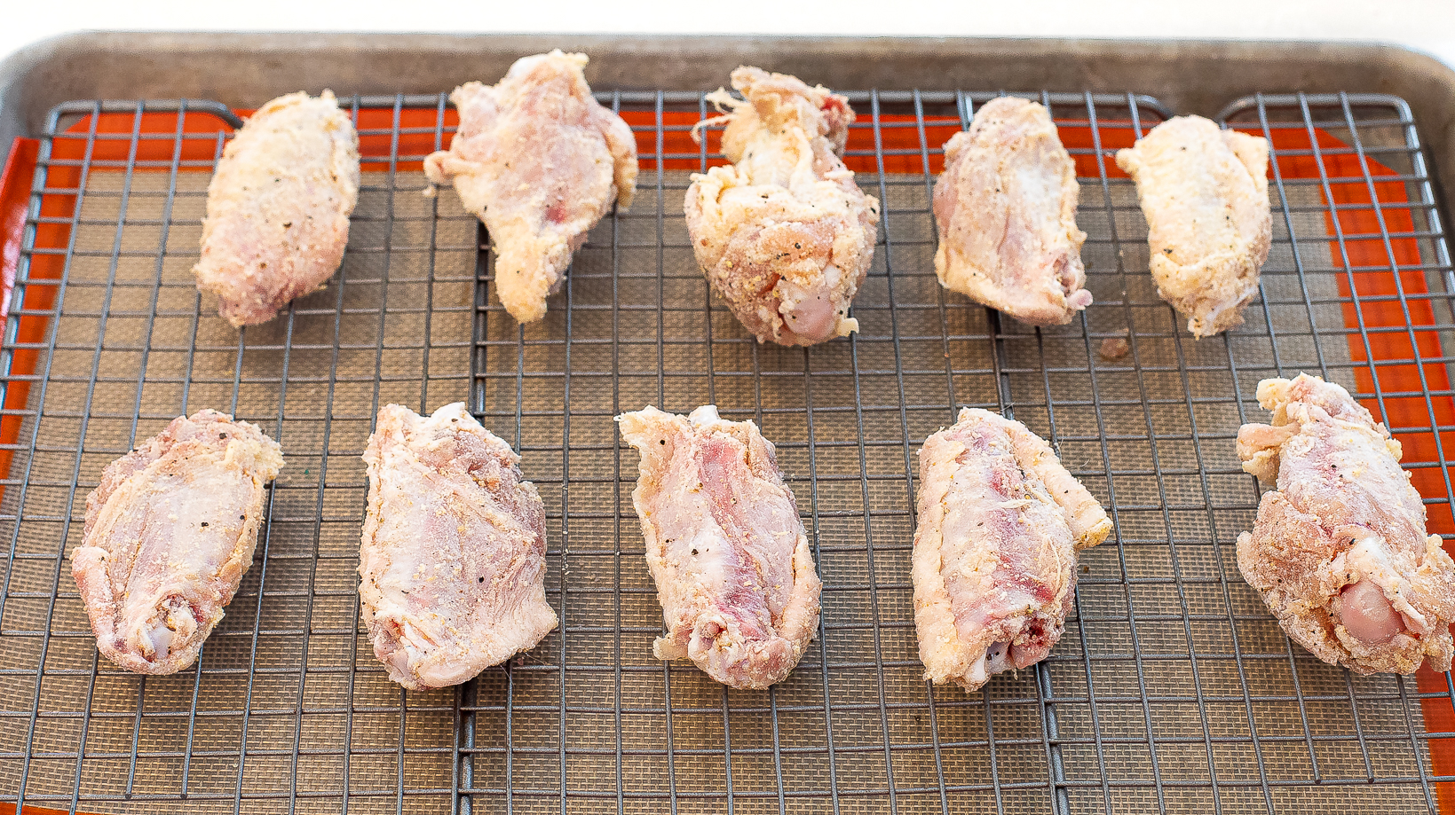 Raw chicken wings on a wire rack lined baking sheet.