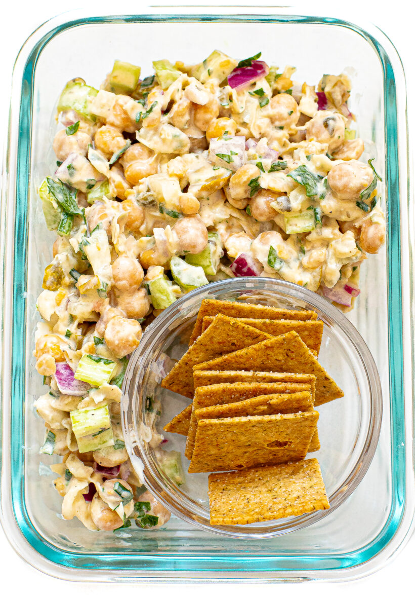 Chickpea salad in a glass container next to a small bowl of crackers.