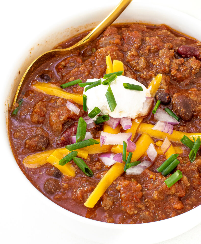 crockpot chili with green onions, red onions, sour cream and shredded yellow cheddar cheese