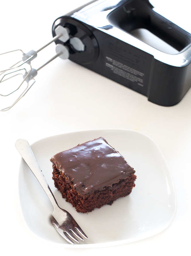 Cake on a white plate with a fork and the hand mixer in the background