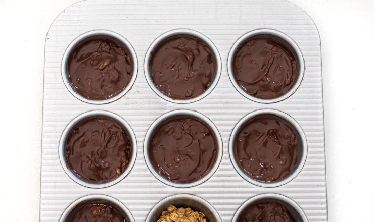 Oat cups topped with a chocolate layer in a muffin tin.