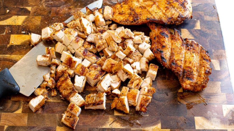 Grilled chicken diced on a cutting board.