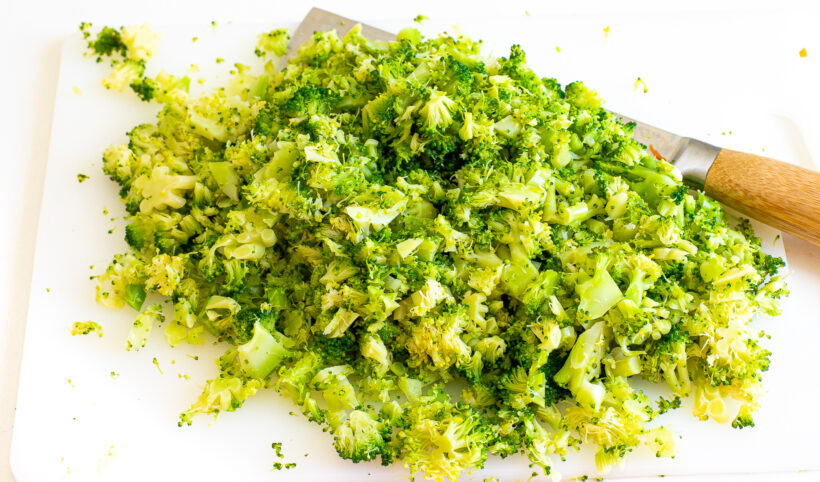 Chopped broccoli on a cutting board next to a large knife. 