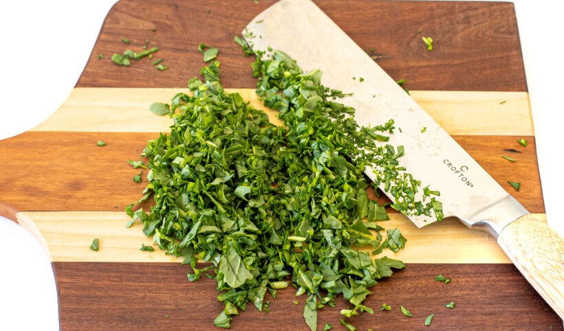 Herbs and arugula being chopped on a cutting board.