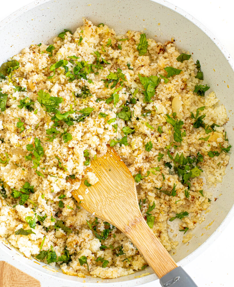 Cilantro lime cauliflower rice in a skillet with a sooden spoon.