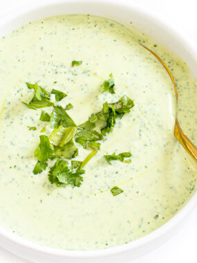 Cilantro sauce served in a white bowl with sprigs of cilantro on top.