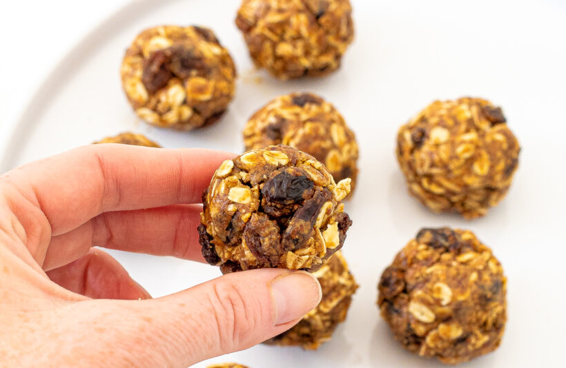 Hand holding a oatmeal raisin energy ball with more in the background. 