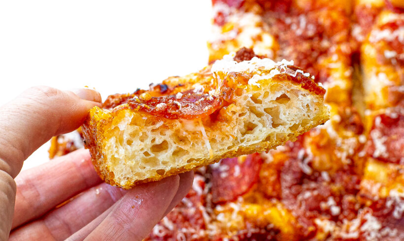 Hand holding up a slice of Detroit style pizza.