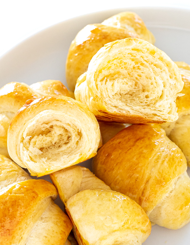 Crescent rolls in a white dish with some crescent roll broken in half. 