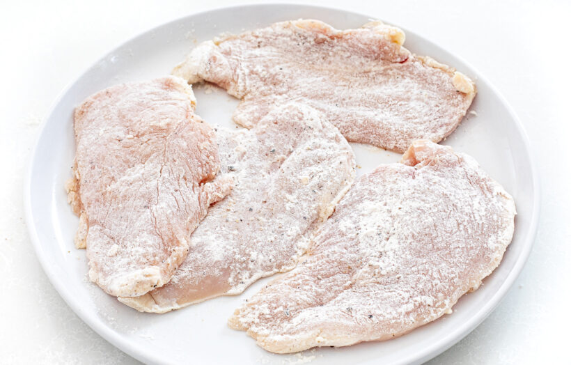 Raw chicken dredged in flour on a white plate.