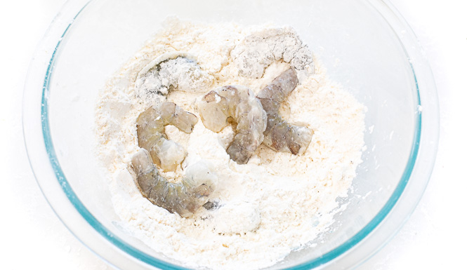 Shrimp being coated in the cornstarch mixture in a mixing bowl. 