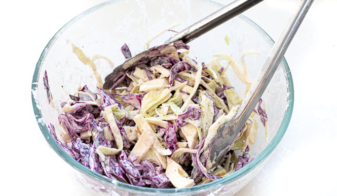 Coleslaw being mixed in a glass mixing bowl. 