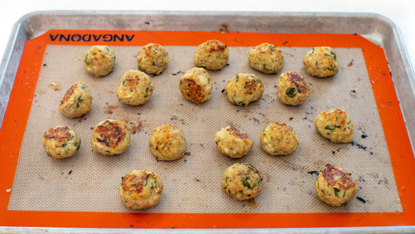cooked chicken meatballs on baking sheet lined with nonstick shipmate