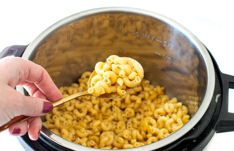 Spoon holding up a spoonful of macaroni above the instant pot.
