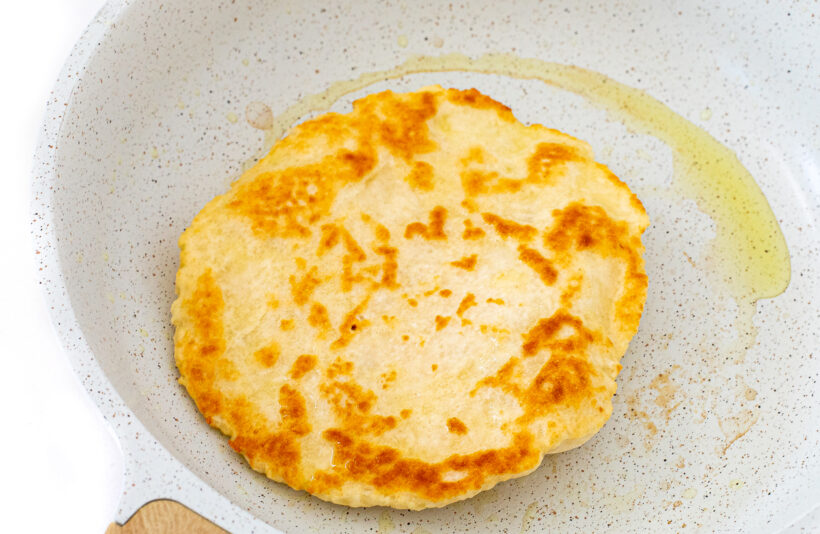Cooked naan bread in a hot skillet with olive oil.