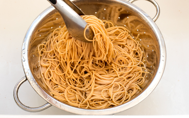 Tongs holding pasta in a collander.