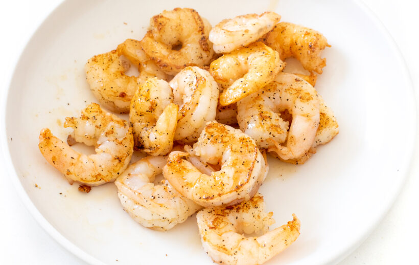 Cooked shrimp set aside on a white plate.